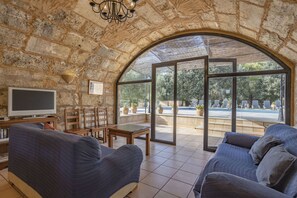 A spacious living area with a stone wall, large arched window, and a view of an outdoor pool area. - 6 bedroom finca with pool and barbecue (Selva)