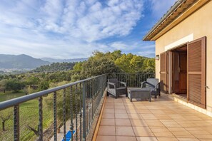 A balcony with outdoor furniture, a view of a green landscape, and a building with a brown door. - 6 bedroom finca with pool and barbecue (Selva)