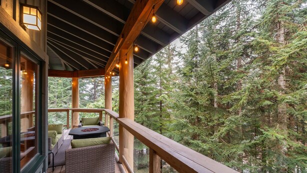 Um deck de madeira com área de estar e lareira, com vista para uma floresta densa.