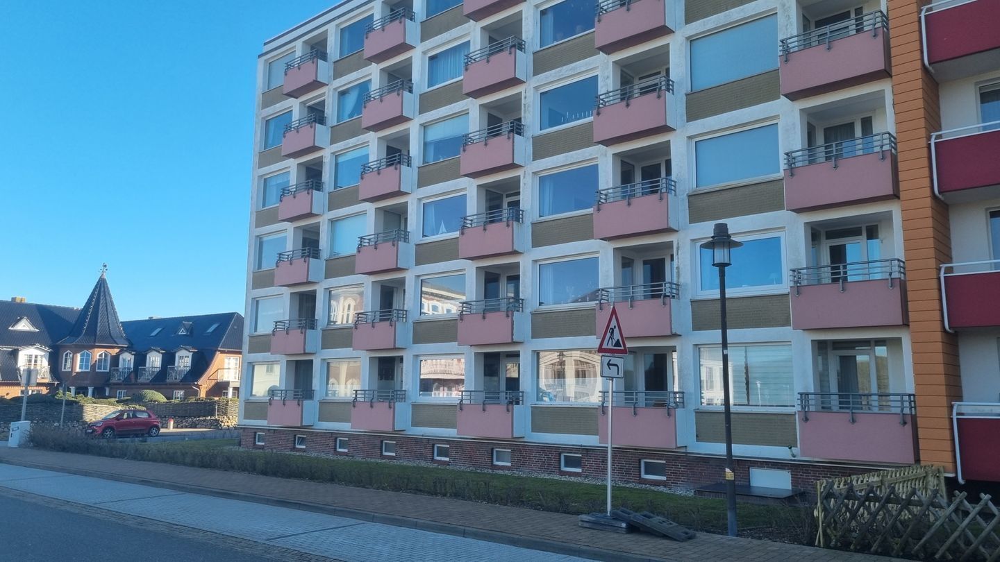 A multi-story residential building with balconies, a pedestrian crossing sign, and a street lamp.