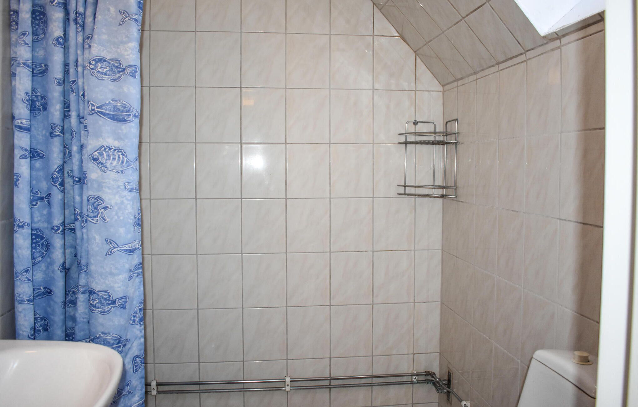 Un baño con ducha, paredes de azulejos, inodoro y lavamanos.