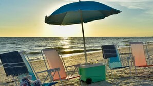 A beach scene with a row of beach chairs and a cooler under a blue umbrella. - Mid Century Home with Heated Pool + Spa (Bonita Springs)