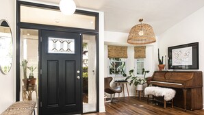 A room with a black door, a piano, a bench, and a hanging light fixture. - Mid Century Home with Heated Pool + Spa (Bonita Springs)