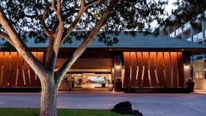 A modern building with a large tree in the foreground, a well-maintained lawn, and a reception area visible through the entrance.