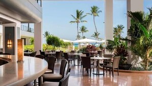 An outdoor dining area with round tables and chairs, surrounded by palm trees and umbrellas. - Marriott Waikoloa Ocean Club 2BR Oceanfront Villa (Waikoloa Beach)