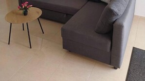 Ein modernes Wohnzimmer mit einem grauen Ecksofa, einem runden Couchtisch mit einer Topfpflanze und einem großen Wandbild mit Tiger-Motiv.