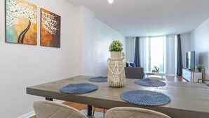 A modern dining area with a long table, blue placemats, and a decorative vase with a plant. - Komffy Apartment w/2 Queen Beds and panoramic view (Sunny Isles Beach)