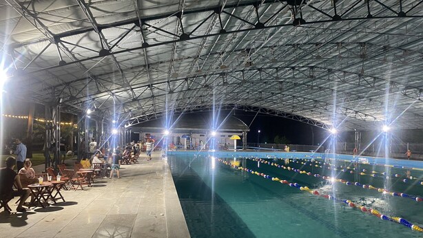 Una piscina interior con techo cubierto, rodeada de zonas de estar y un bar junto a la piscina.