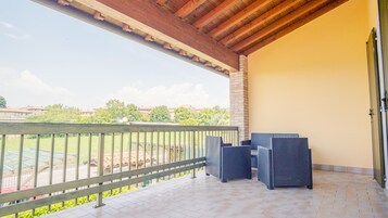 A covered balcony with a view of a sports field, a brick wall, and two wicker chairs.