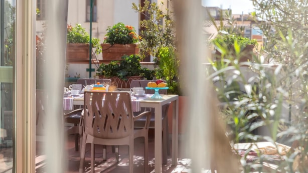 An outdoor dining area with a table set for two, surrounded by potted plants and a view of buildings. - Liberty 13 in Sassari (Sassari)