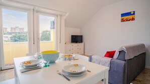 Ein Essbereich mit einem Tisch für zwei Personen, einer Couch und einem Fernseher im Hintergrund.