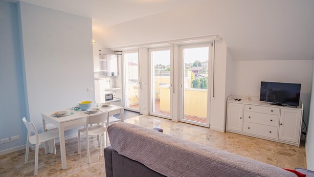 Eine moderne Wohnung mit Essbereich, einer Couch, einem Fernseher und einem Balkon mit Stadtblick.