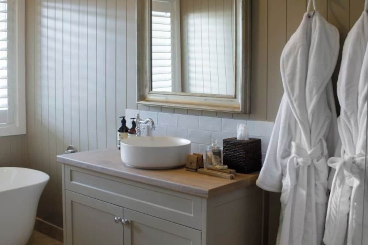 Un baño con lavamanos blanco, espejo y toallero.
