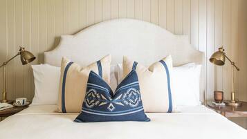 Cama bem arrumada com cabeceira branca, duas luminárias de mesa e travesseiros decorativos.