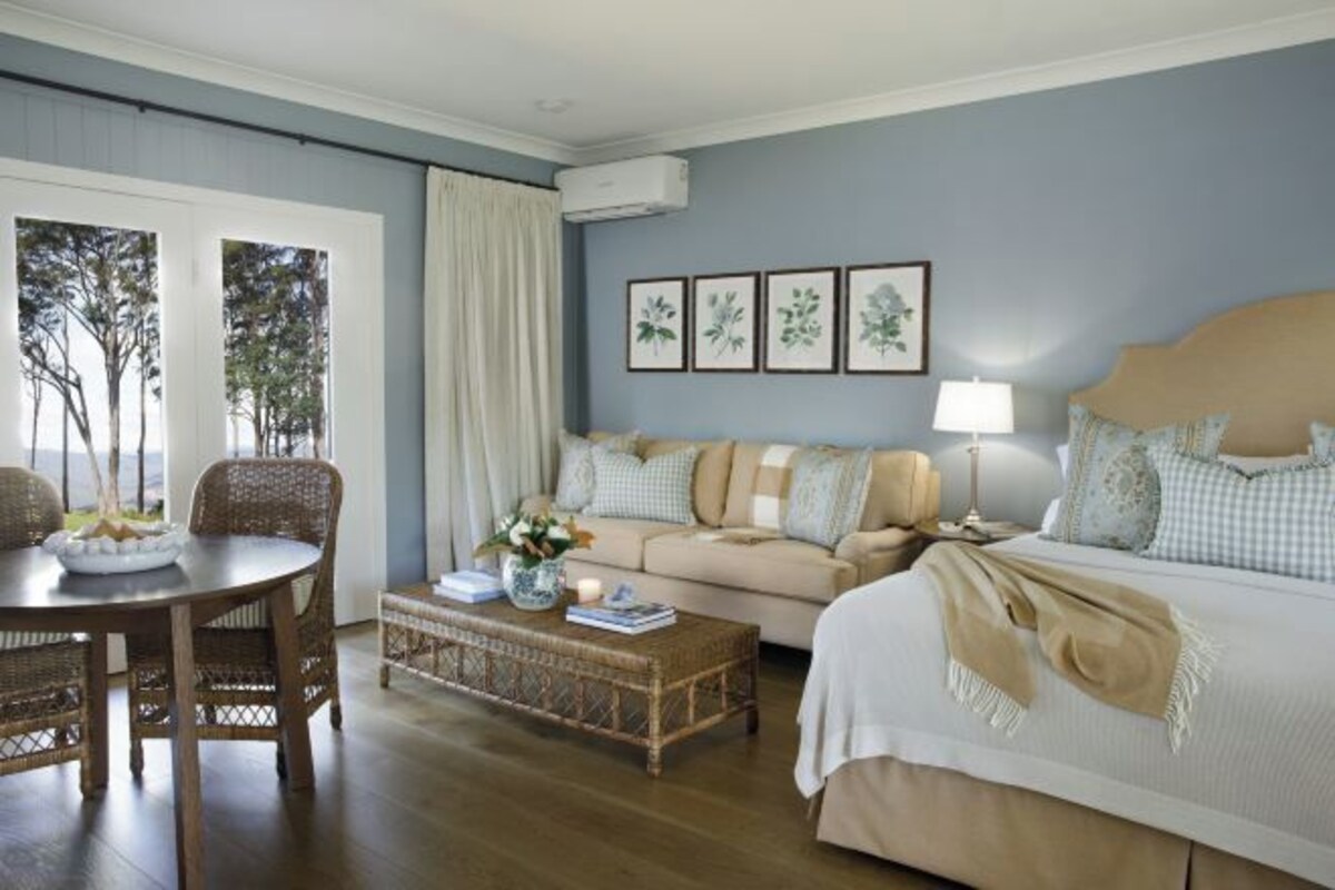 Una habitación con sofá, cama, mesa de comedor con sillas, una mesa auxiliar y láminas botánicas enmarcadas en la pared.