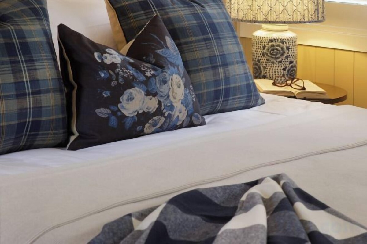 Una cama con un colchón blanco, almohadas estampadas en azul y negro, y una colcha.