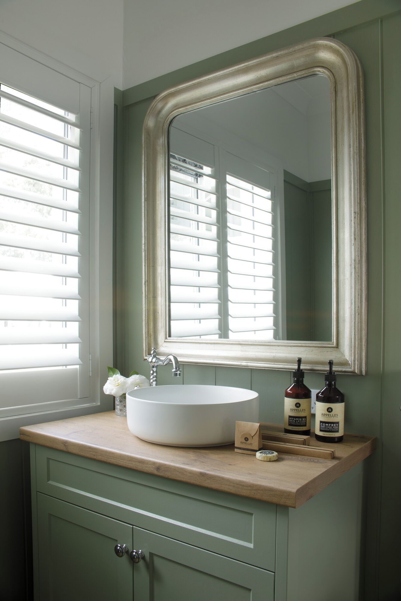 A bathroom with a white sink, a mirror, and two bottles of Apelles hair care products on the counter.
