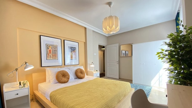 Une chambre à coucher moderne avec un lit, des tables de chevet, un luminaire suspendu et des tableaux encadrés accrochés au mur.