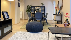 Un salon moderne comprenant un coin repas, un pouf noir, une lampe sur pied et un miroir mural.