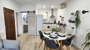 A modern kitchen with a central island, a dining area with a round table and chairs, and a grey sofa in the living area. - Minichalet Jacaranda with swimming pool, garden and barbecue. (Chiclana)
