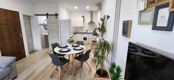 Una cocina moderna con armarios blancos, una isla central y una zona de comedor con una mesa redonda y sillas.