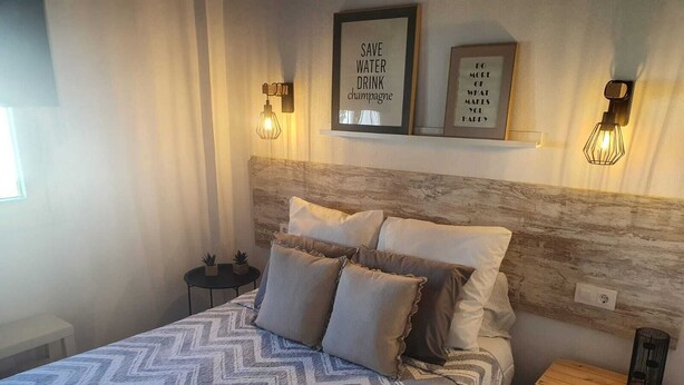 A bedroom with a bed, a nightstand, and wall-mounted light fixtures. - Minichalet Jacaranda with swimming pool, garden and barbecue. (Chiclana)