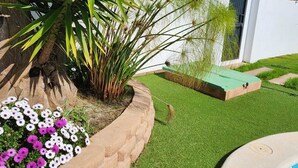 A well-maintained garden with a pool, a palm tree, and a white building with a modern design. - Minichalet Jacaranda with swimming pool, garden and barbecue. (Chiclana)