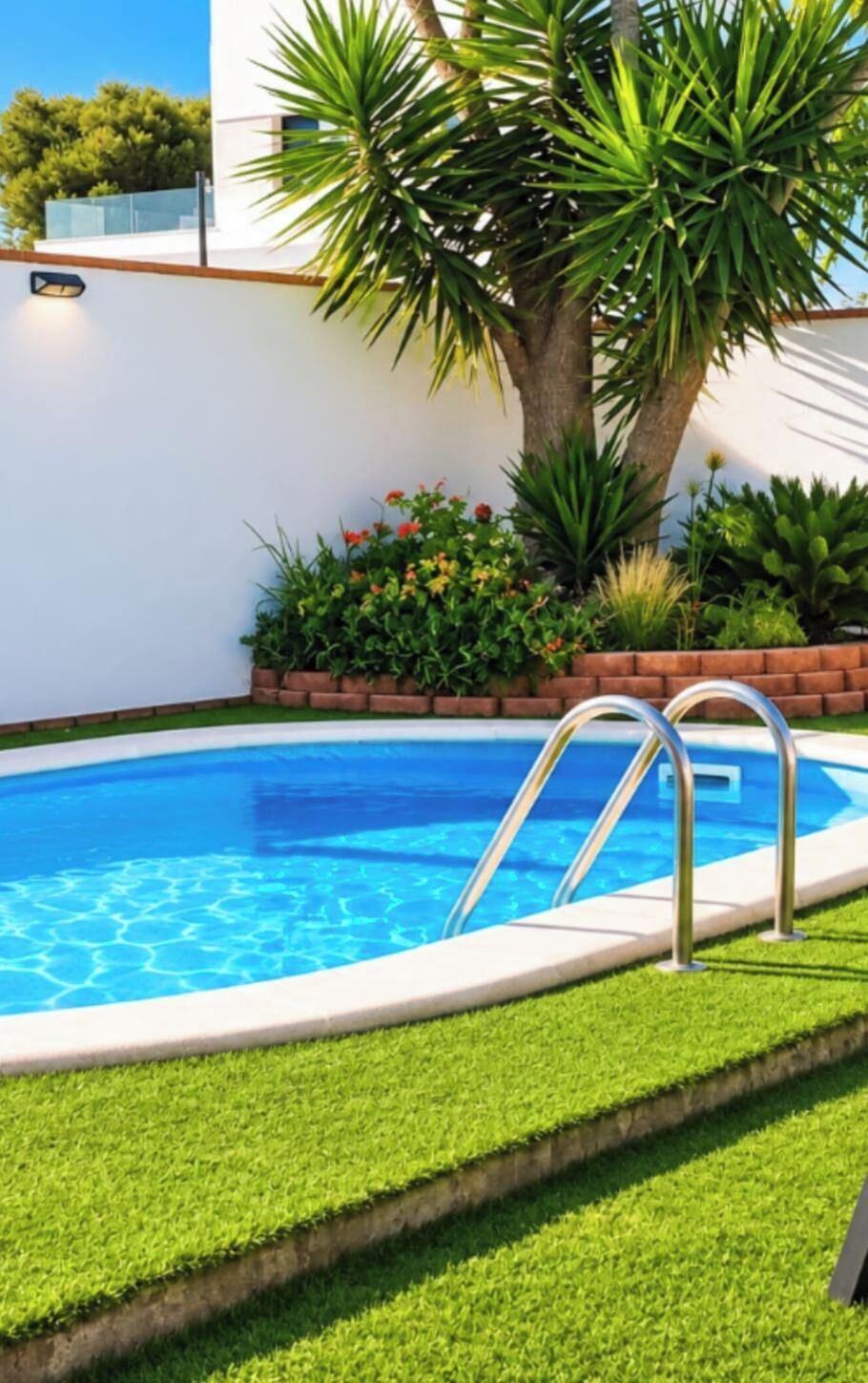 Piscina com escada de metal, cercada por um muro de tijolos e grama verde.