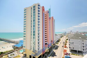 A multi-story hotel with balconies, a beach view, and a pier extending into the ocean.
