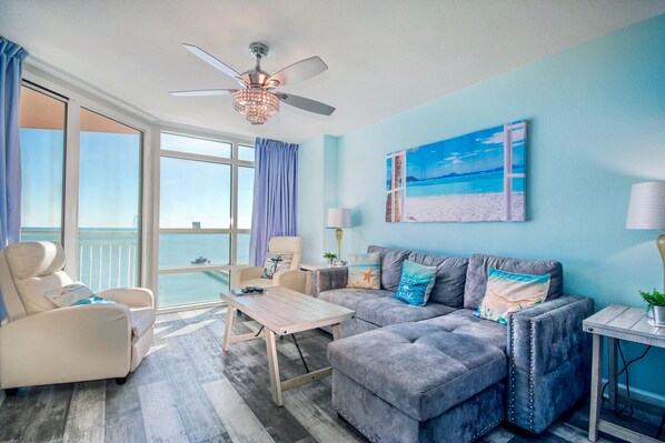 A room with a balcony, a ceiling fan, a sofa, a chair, and a table.
