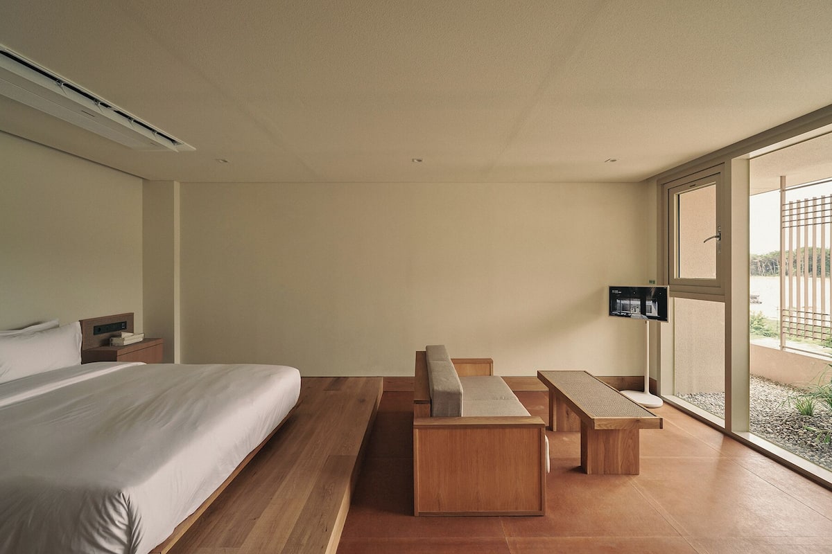 Une chambre d’hôtel avec un lit, un bureau et un banc. Il y a une fenêtre donnant sur l’extérieur.