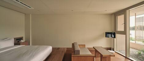 Habitación de hotel con cama, escritorio y banco. Se ve una ventana con vistas al exterior.