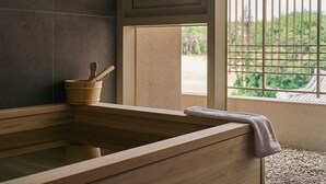 A wooden bathtub with a towel, a wooden bucket, and a window with a view of greenery. - IJE Gyeongju (Gyeongju)
