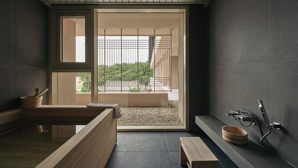 A modern bathroom with a wooden bench, a bathtub, and a window with a view of greenery. - IJE Gyeongju (Gyeongju)