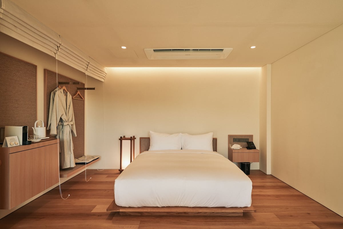 Une chambre d’hôtel moderne dotée d’un grand lit, d’un parquet, d’un bureau intégré, d’un porte-peignoir et d’une petite table de chevet avec un téléphone et une lampe.