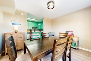 A dining area with a wooden table and chairs, a kitchen in the background, and a sign on the wall. - Sophisticated, bay-view home with pool, deck, W/D, grill & AC - close to beach (South Padre Island)