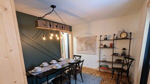 A dining area with a wooden table set for four, a world map on the wall, and a shelf with clocks and decorative items. - Magical Northern Michigan Cottage with Hot Tub (Bear Lake)