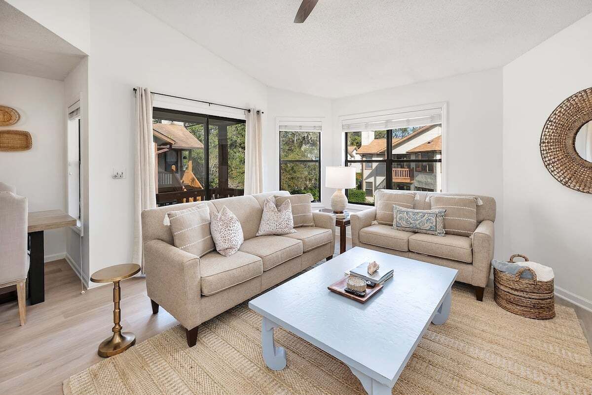 Ein geräumiges Wohnzimmer mit zwei beigefarbenen Sofas, einem Couchtisch und einem großen Fenster mit Blick auf ein Haus.