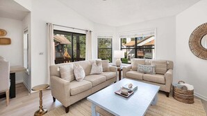 Uma sala de estar ampla com dois sofás bege, uma mesa de centro e uma grande janela com vista para uma casa.
