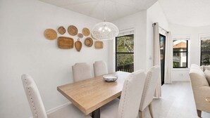 Uma sala de jantar com uma mesa de madeira, cadeiras estofadas brancas e decorações de parede em tecido.