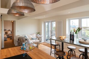 Une cuisine moderne avec une table en bois, des tabourets de bar et une vue sur l’extérieur grâce à de grandes fenêtres.