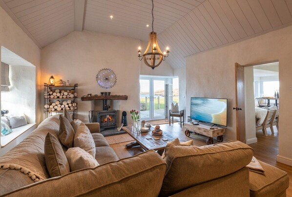A spacious living room with a large sofa, a fireplace, a television, and a view of the outdoors.