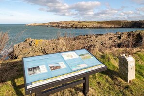 An informational sign near a coastal area with rocky terrain and a body of water.