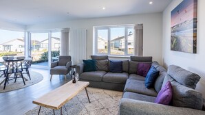 A modern living room with a grey sofa, a wooden coffee table, and a dining area with a table and chairs.