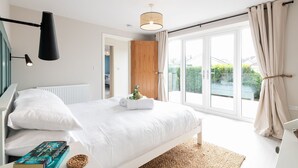 A modern bedroom with a large bed, a bedside lamp, a hanging light fixture, and a view of the outdoors through a sliding glass door.