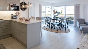 A modern kitchen with a central island, a dining area with a round table and chairs, and a view of the outdoors through large windows.