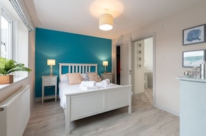 A bedroom with a white bed, two bedside tables, a teal accent wall, and a ceiling light fixture.
