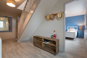 A staircase leading to a bedroom with a blue wall, a wooden console table with shoes, and a fire extinguisher.