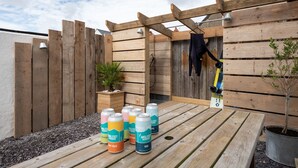 A wooden deck with a table holding cans of Anglesey Brewery, a wooden fence, and a potted plant. - Kittiwake Cottage : Stylish 2‑Bed Pet-Friendly Cottage in Rhosneigr | Managed by Anglesey Holiday Le (Rhosneigr)