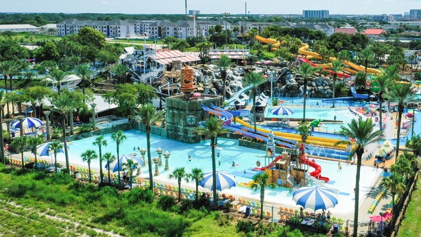 Ein Wasserpark mit mehreren Becken, Wasserrutschen und einem großen, von Palmen umgebenen Mittelbecken.